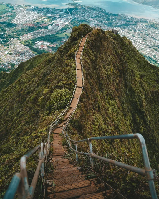 A steep staircase follows a green mountain ridge above a coastal town.